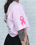 Woman wearing a pink t-shirt with a breast cancer awareness ribbon against a white brick wall. Garage Men's Grooming Merchandise. 